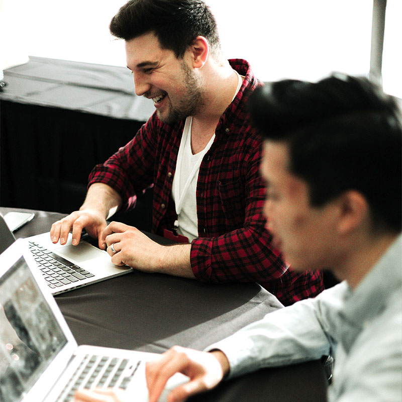 Two men smilling and working on laptops